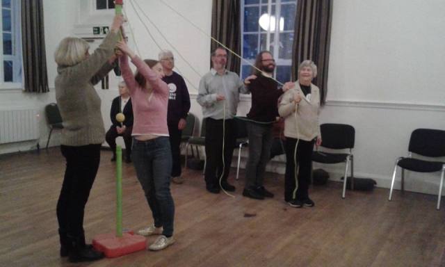 Denise, Wayne, Andy and Dave explore staging possibilities. Each stands behind the other in a line holding a rope attached to a central post, like a maypole, which Jenni and Steph are holding.
